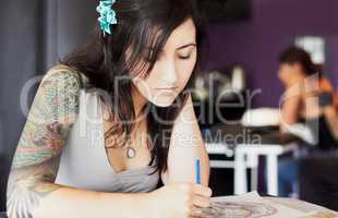 Coming up with some great designs. A female tattoo artist drawing a new design while in her tattoo parlour.