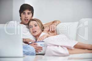 This is too tense. Shot of a young couple watching a scary movie at home.