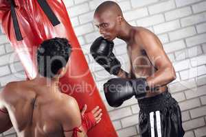 Bringing out his killer instinct. Two boxers practicing on a punching bag together.