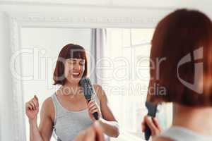 I feel like a rockstar today. Shot of an attractive young woman holding a hairbrush and singing in her bathroom at home.