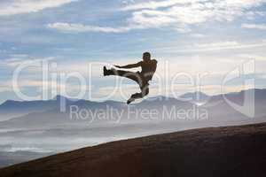 Precision technique on the mountain. A male kickboxer flying through the air as he practises his fly kick technique.