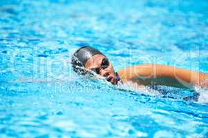 Training to be the best. Female swimmer making her way through a swimming pool stroke by stroke.