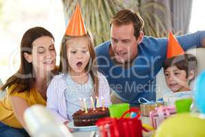 The moment theyve all been waiting for. Shot of a little girl blowing out the candles of her birthday cake surrounded by her family.