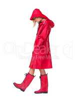 Why does it always rain on me. Woman wearing a red raincoat, hat and boots with her head looking down and hands in her pockets- full length.