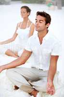 Letting their worries wash away - Meditation. A young couple meditating in the lotus position on the beach.