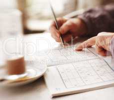 Woman trying to solve Sudoku Puzzle - window, sunlight, and coffee. Woman trying to solve Sudoku Puzzle - window, sunlight, and coffee.