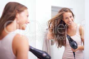 Taking care of her luscious mane. A young woman blow drying her hair in front of a mirror.
