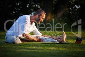 Online workouts- from beginner to advanced. Shot of a mature man looking at online instructions on his tablet while doing yoga.