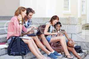 Modern study group. Young teens out on their college steps sharing notes and information on their laptops.