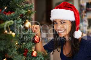 Shes a pro at Christmas tree decoration. Portrait of a beautiful young woman decorating a Christmas tree.