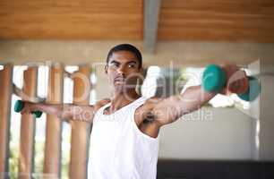 The body achieves what the mind believes. A handsome young african man lifting dumbells indoors.