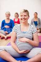 My focus is on a calm birth. A group of pregnant women sitting cross-legged in a yoga class and smiling happily.