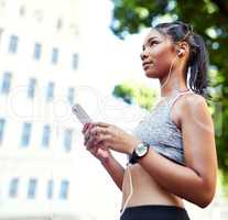 This song always gets me in an active mood. Shot of an attractive young woman listening to music and using her cellphone while exercising outdoors in the city.