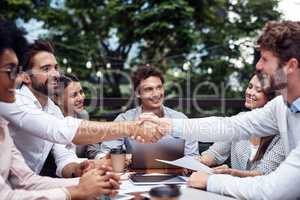 Sealing the deal. Cropped shot of two handsome young businessmen shaking hands while sitting with their colleagues outdoors.