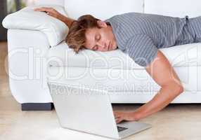 High-speed connection for couch potatoes. A young man lying on his couch with his hand resting on his laptops keyboard.