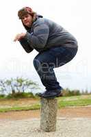 Ready to pounce. An overweight young man in winter wear balancing playfully on a post.