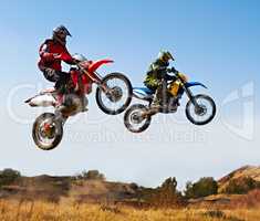 Nothing compares to the thrill of a good race. Action shot of two dirt bikers jumping with their bikes over a field.