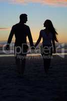 The best thing about sunsets is watching them with you. Silhouette shot of a young couple walking on the beach.