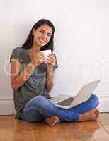 Wireless connectivit. Shot of a young woman sitting on the floor at home drinking a coffee and using a laptop.