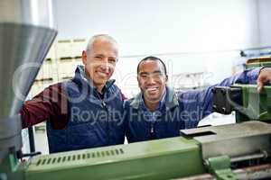 Together we make this machine run smoothly. Shot of two men working over factory machinery.