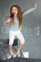 This one goes out to my fans. Shot of a cute little girl jumping on a bed while pretending to sing into a hairbrush.