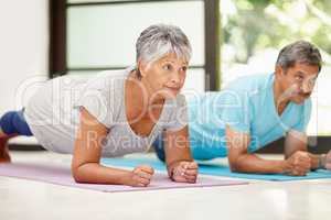 We keep each other focused on fitness. Shot of a mature couple exercising together at home.