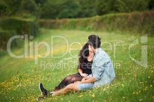 Springtime romance. Cute young couple sitting in a springtime field kissing.