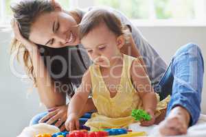 Shes a little genius already. Shot of a cute baby girl sitting on the floor with her mom and playing with toys.