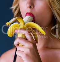 Something tasty to satisfy the craving. Cropped studio shot of a young woman eating a banana suggestively against a dark background.