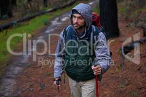 Using nature to keep fit. Shot of a handsome man hiking in a pine forest using nordic walking poles.