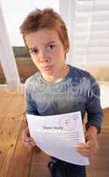 F is for failure. Shot of a sulking young boy holding up a paper that got him an F.