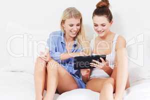 The ease of touchscreen technology. Two pretty young woman using a tablet to browse the internet while relaxing in bed.