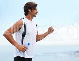 Nothing can hold him back. Profile view of a handsome man holding a water bottle, going for a run and listening to music - copyspace.