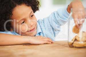 Mmm, so many cookies just for me. A cute young boy grabbing a cookie from the cookie jar.