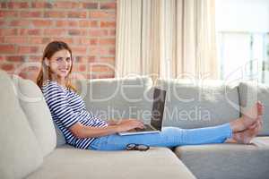 My home is a wifi hotspot. Shot of a young woman using a laptop on her sofa at home.