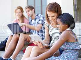 Technological teens. Young teens looking at their laptops and digital tablets as they socializing outdoors.