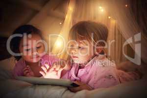 Its time for some bedtime magic. Shot of two little girl using a digital tablet at their sleepover.