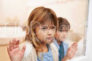 Trapped in a glass box of emotion. Shot of two unhappy-looking young children looking out a window on a rainy day.