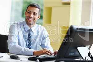 Working with a smile. A smiling young businessman sitting at his desk and working.