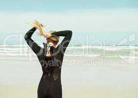 Tying back her hair for comfort during surfing. A surfer girl tying her hair into a ponytail.