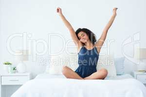 Rise and shine. Shot of an attractive young woman sitting up in bed and stretching with her arms raised in the morning.