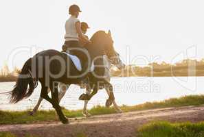 No one can teach riding so well as a horse. Shot of two unrecognizable women riding their horses outside on a field.