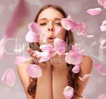 Filling the air with a whimsical scent. Gorgeous young woman blowing away a handful of rose petals on a pink background.
