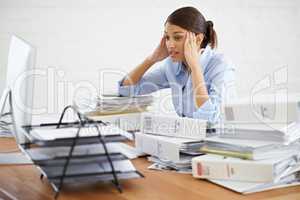 My brain is going to explode soon.... A young businesswoman looking overwhelmed while surrounded by paperwork.