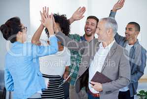 Successful and loving it. Shot of a group of happy coworkers high-fiving while standing in an office.