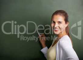 Shaping the future generation. A beautiful young teacher writing on a blackboard while smiling at the camera - copyspace.