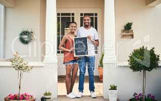 We bought our first house. Portrait of a young couple holding a chalkboard with our first home written on it.