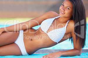 Summer beauty. Young woman reclining by the side of a swimming pool with a smile.