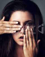 She has an intense character to go with her beauty. Studio portrait of an attractive young woman posing with her hands covering her face against a grey background.
