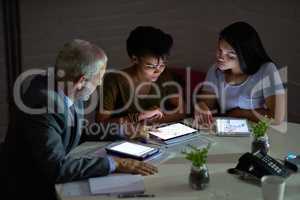 Combining their technical knowhow. Shot of a group colleagues using digital tablets while working late in an office.